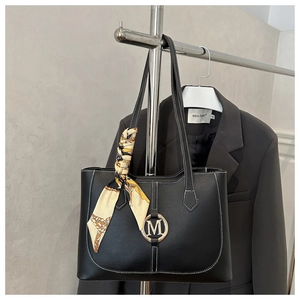Detail of black tote bag featuring white stitching, metal M logo, and floral silk scarf