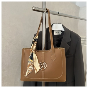 Close-up of brown leather tote bag with metal M logo and elegant silk scarf detail