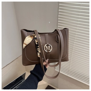 Detail of brown leather tote bag featuring a gold M-buckle and silk scarf wrapped handle