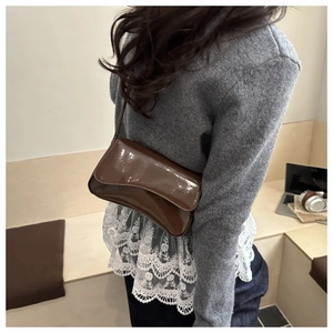 Detail einer tiefbraunen Baguette-Tasche aus Lackleder, von einem Model lässig getragen