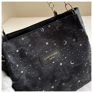 Detail of black tote bag with silver star moon patterns and gold chain handles