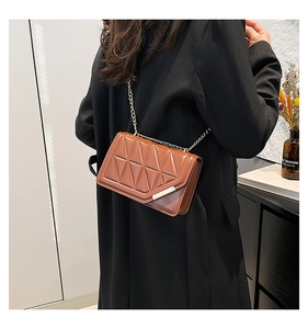 Detail of brown quilted crossbody bag with golden chain strap on a black coat