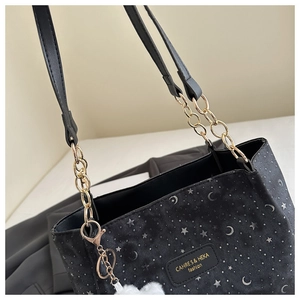 Detail of black canvas tote with silver star prints, gold chain strap, and plush charm