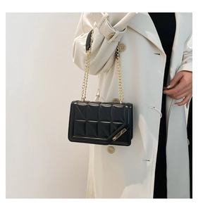 Close-up of black quilted small square bag featuring gold chain strap and metal trim