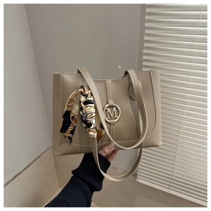 Detail of khaki tote bag featuring an M-letter metal ornament and a patterned silk scarf handle