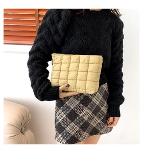 Detail einer beige gesteppten Puffer-Clutch mit quadratischem Muster von einem Model gehalten