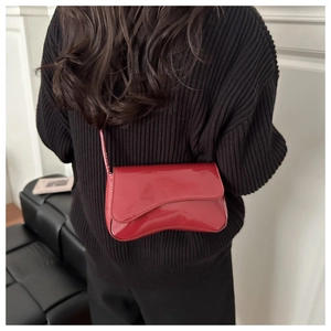 Detail der roten Lackleder-Baguette-Tasche über einem schwarzen Pullover für den Winter