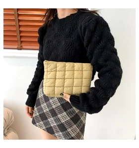 Detail einer beigen gesteppten Clutch, gezeigt zu einem schwarzen Pullover und Karorock