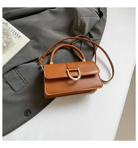 Detail of caramel leather handbag with gold horseshoe buckle on a minimalist background