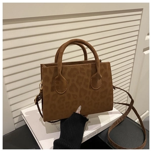 Détail du sac à bandoulière léopard avec garniture dorée et bandoulière réglable sur un livre