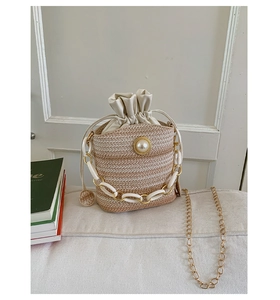 Detail of woven straw bucket bag with large pearl charm and acrylic chain handle