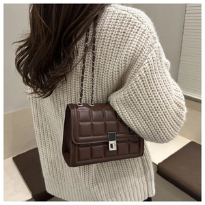 Deep brown checkered crossbody bag with silver chain strap worn over a beige knit sweater