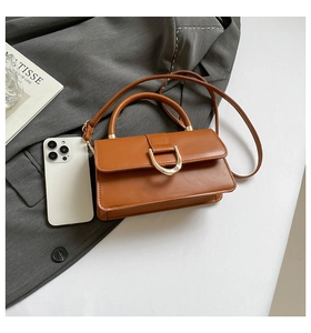 Close-up of brown leather handbag with gold D-ring buckle next to a smartphone