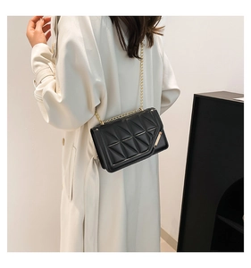 Detail of black quilted crossbody bag with gold chain and metal trim on fashion model