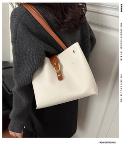 Detail of a white tote bag featuring a brown shoulder strap and golden horsebit buckle