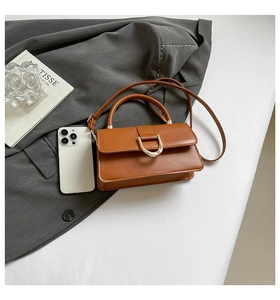 Close-up of caramel brown handbag with golden D-ring buckle on white surface