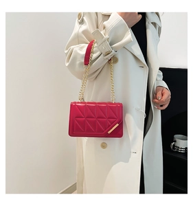 Detail of red quilted small square bag with gold chain strap on a white trench coat