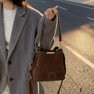 Retro dark brown suede bucket bag with gold hardware for women shown in warm sunset street light