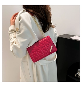 Detail of red quilted square bag with geometric texture and gold chain on model