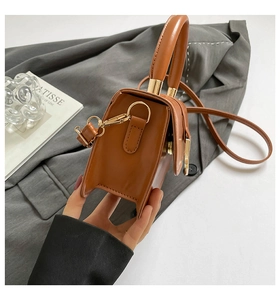 Detail view of structured brown faux leather handbag with elegant gold hardware and top handle