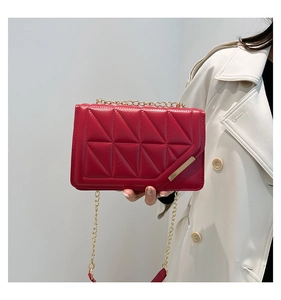 Detail of red quilted crossbody bag with gold chain and glossy faux leather texture