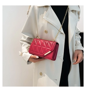 Detail of red quilted chain crossbody bag with golden hardware on beige trench coat