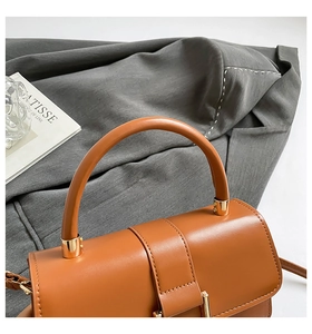 Detail of brown leather handbag with golden hardware and a sleek curved handle