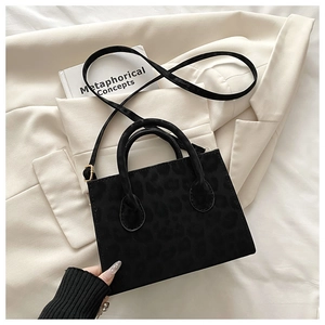 Détail du sac bandoulière noir avec motif léopard embossé et doubles anses sur beige