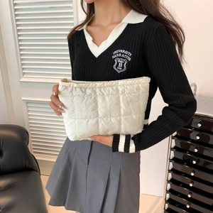 Pochette matelassée blanche avec fermeture éclair dorée tenue par un mannequin en intérieur