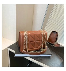 Close-up of brown quilted faux leather shoulder bag with gold chain strap on black books