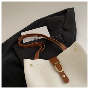 Détail du sac cabas en cuir crème avec lanières brunes et rivets sur un blazer noir