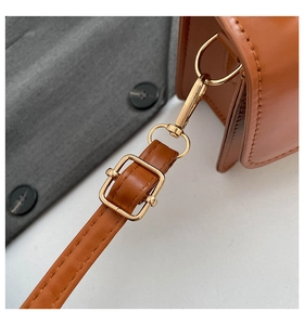 Detail of brown leather strap with golden metal clasp and fine stitching on shoulder bag