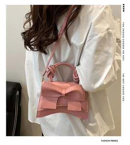 Detail van roze handtas met strik, gevlochten handvat en schouderriem op een model