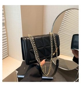 Close-up of black quilted shoulder bag with gold chain strap held against neutral wall