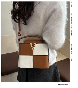 Detail view of contrast color stitching and golden V-shaped buckle on a crossbody bag