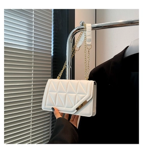 Close-up of white quilted handbag featuring geometric triangle stitching and gold chain strap