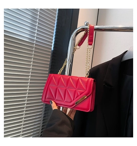 Detail of red quilted square bag with gold metal clasp and chain strap on silver stand