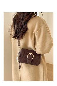 Detail of dark brown suede crossbody bag with gold U-buckle and tassel on wool coat