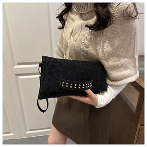 Dettaglio di una pochette leopardata nera con rivetti dorati tenuta da una modella in luce