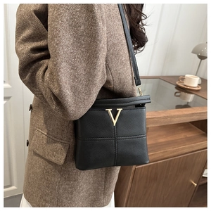 Detail of black lychee grain leather handbag featuring golden V-logo and crossbody strap