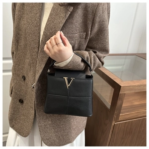 Detail of the black pebbled leather handbag with a golden V logo held by a model
