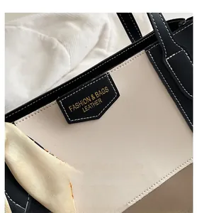 Detail of contrast stitching and leather brand tag on a two-tone tote bag with scarf