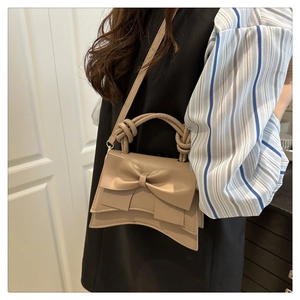 Detail van beige schoudertas met strik, verstelbare riem en knoopvormig handvat