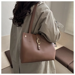Detail of caramel faux leather tote bag with gold metal buckle on female model in a trench coat