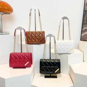 Quilted crossbody chain bags in red, brown, black and white on a geometric display stand
