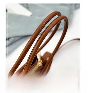 Macro shot of brown leather bucket bag handles with fine stitching and gold metal zipper