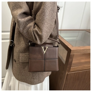 Close-up of a dark brown pebble leather crossbody bag with a gold metal V-logo hardware