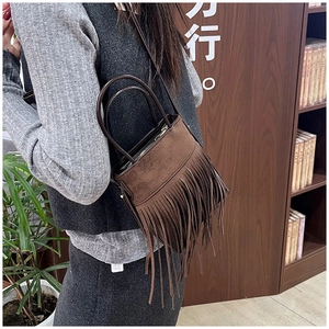 Detail of bohemian dark brown suede bucket bag featuring long fringes and cross-body strap