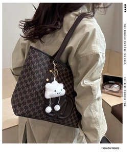 Close-up of brown leather tote bag featuring debossed M logo and white plush cloud charm