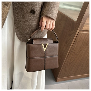 Detail of a brown leather handbag featuring a gold V-shaped buckle and fine lychee texture